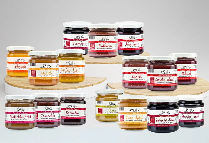 Verschiedene Gläser mit hausgemachten Fruchtaufstrichen vom Familienbetrieb Haselberger im Weinviertel. Sorten wie Erdbeere, Himbeere, Brombeere, Ribisel, Kirsche, Marille, Pfirsich, Birne, Zwetschke, Hollunder-Birne und weitere sind dekorativ auf Holzpodesten angeordnet